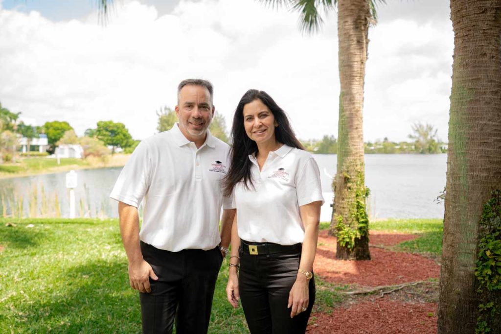 International College Counselors Founder Mandee Heller Adler stands with partner Barry Liebowitz outdoors in front of a palm tree and lake.